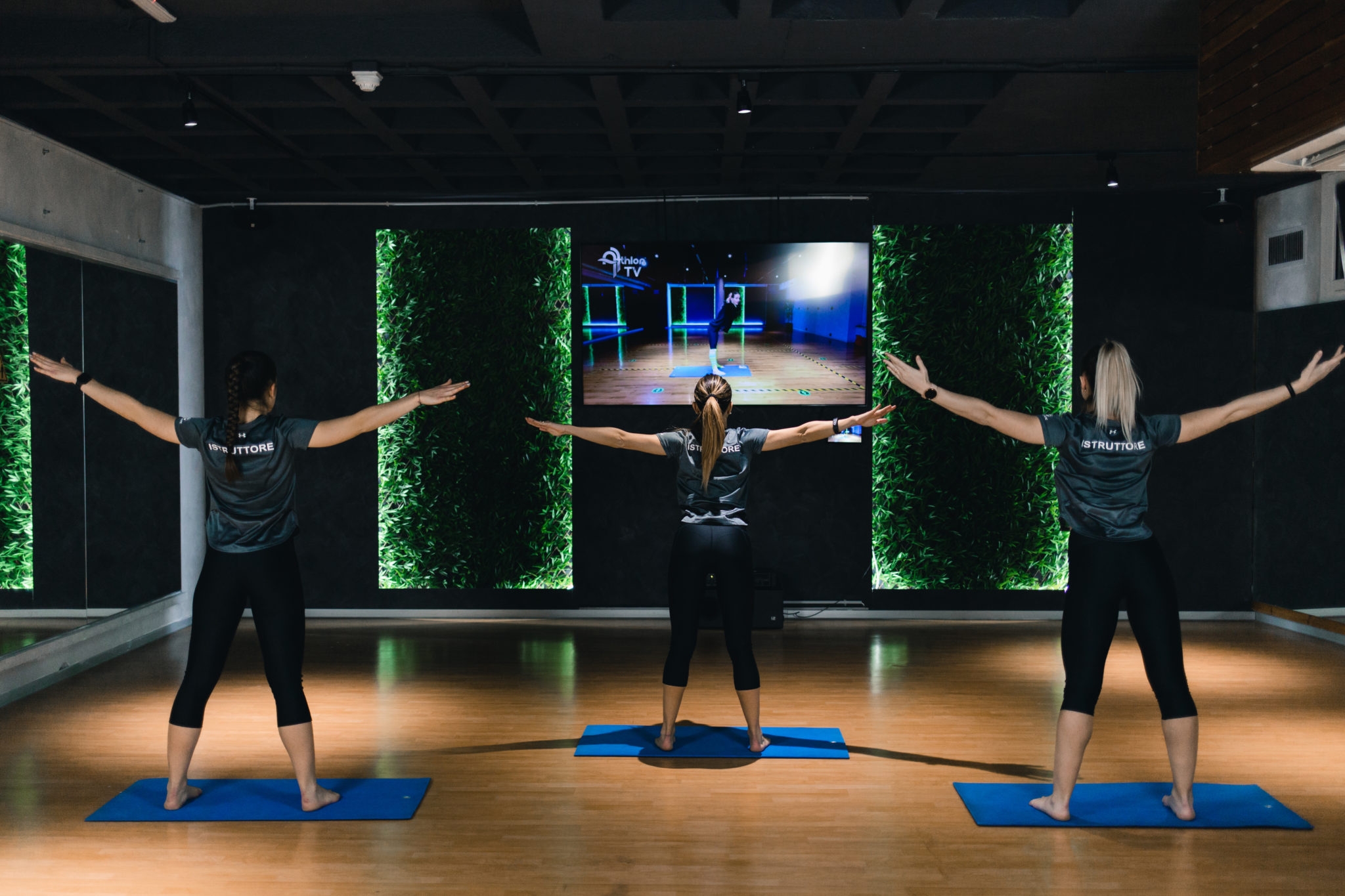 three women in black clothes at the gym working out in front of the television